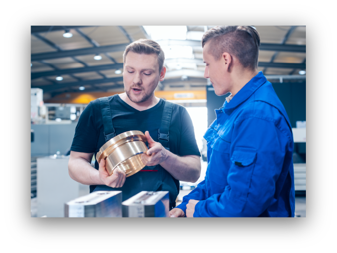 Two men discuss a metal part Two men discuss a metal part